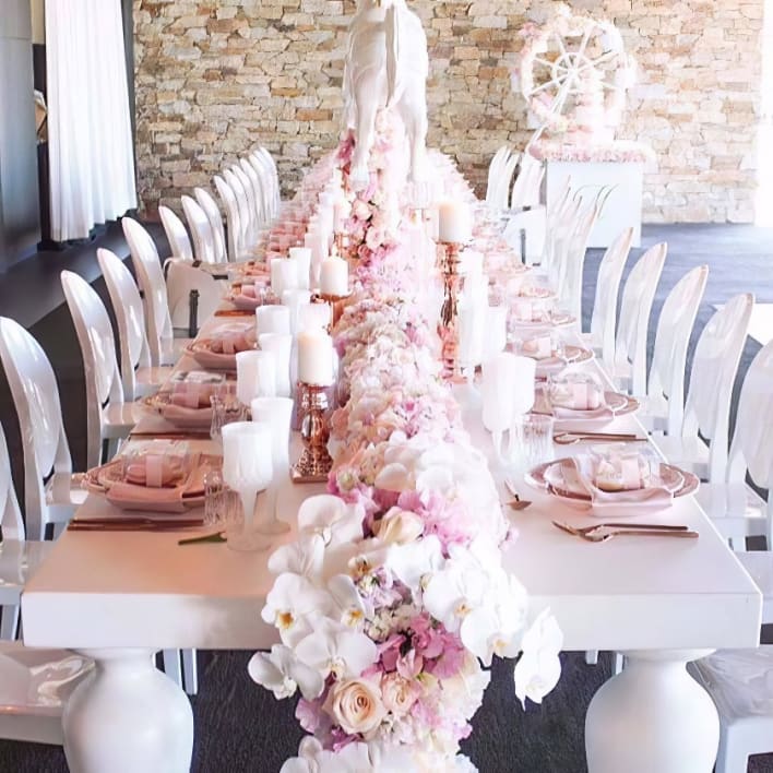 A white table with pink flowers and white chairs.