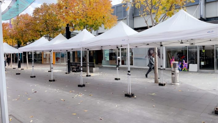 A group of white tents on a sidewalk in front of a store.