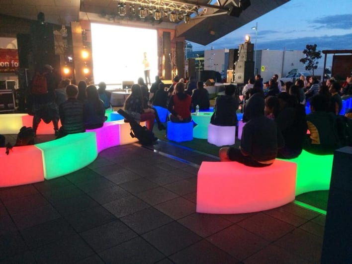 A group of people sitting on a bench in front of a screen.