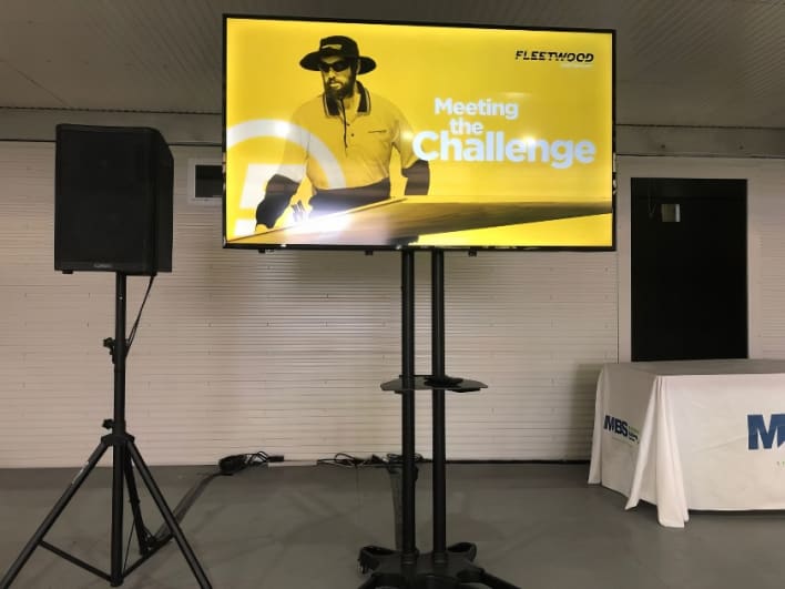 A large tv screen with a man standing in front of it.