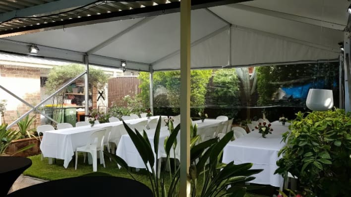 A white tent with tables and chairs set up in a backyard.