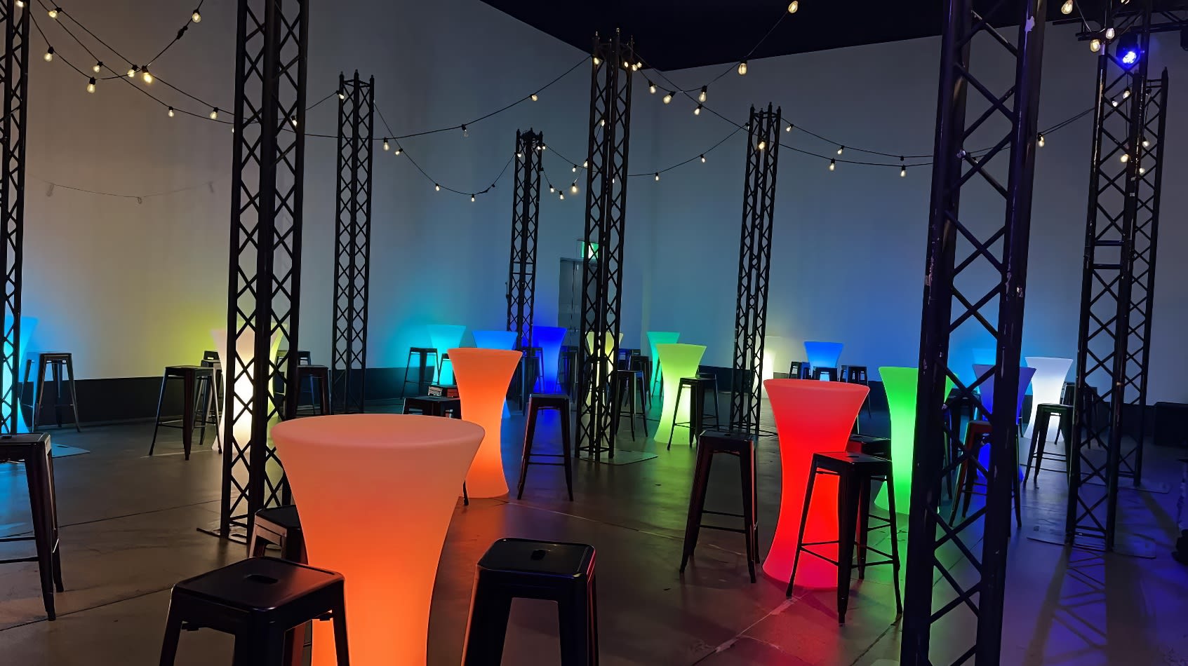 A room filled with colorful lights, stools, and Black Tolix Stool Hire.