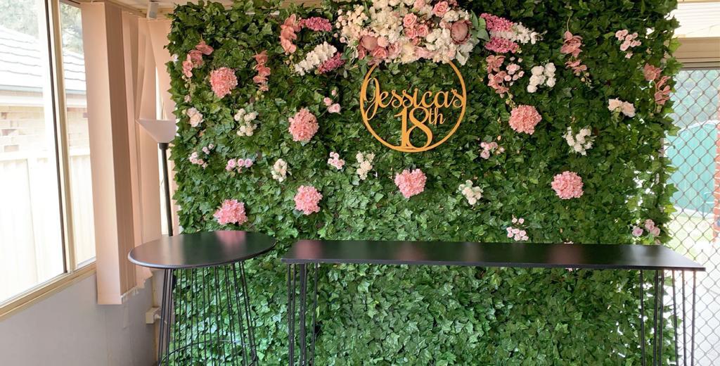 A vibrant green wall adorned with colorful flowers, complemented by a sleek table in front of it.