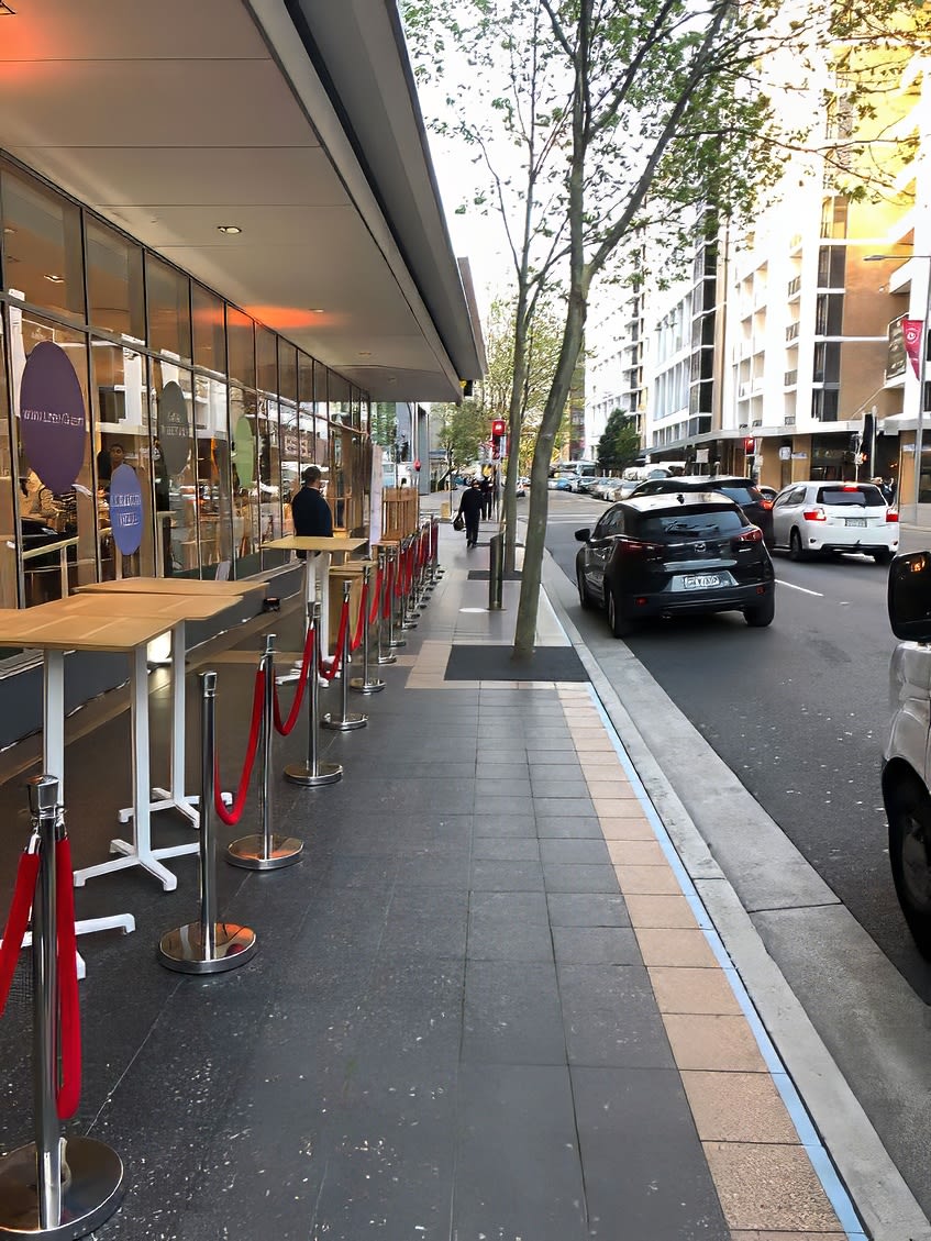 A sidewalk with tables and chairs in front of a building, offering a charming outdoor seating arrangement.