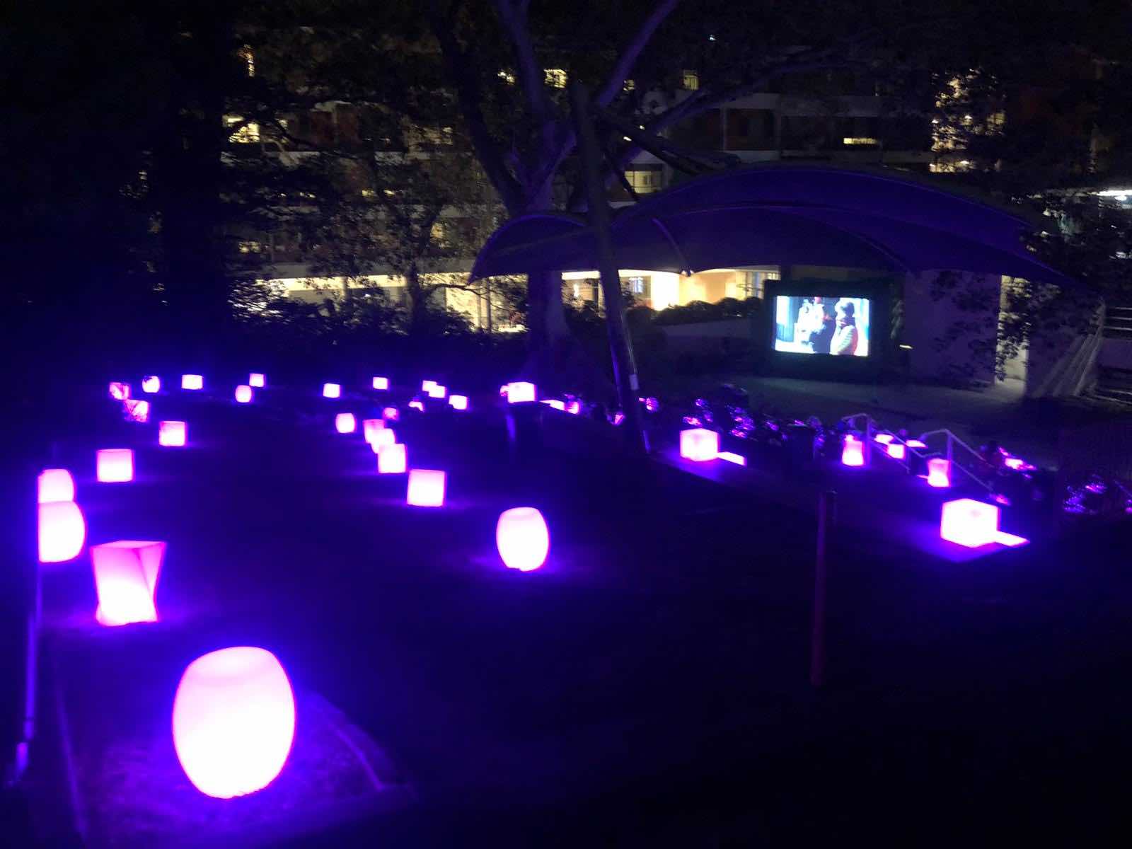 A cluster of purple lighted urns illuminating a grassy area.