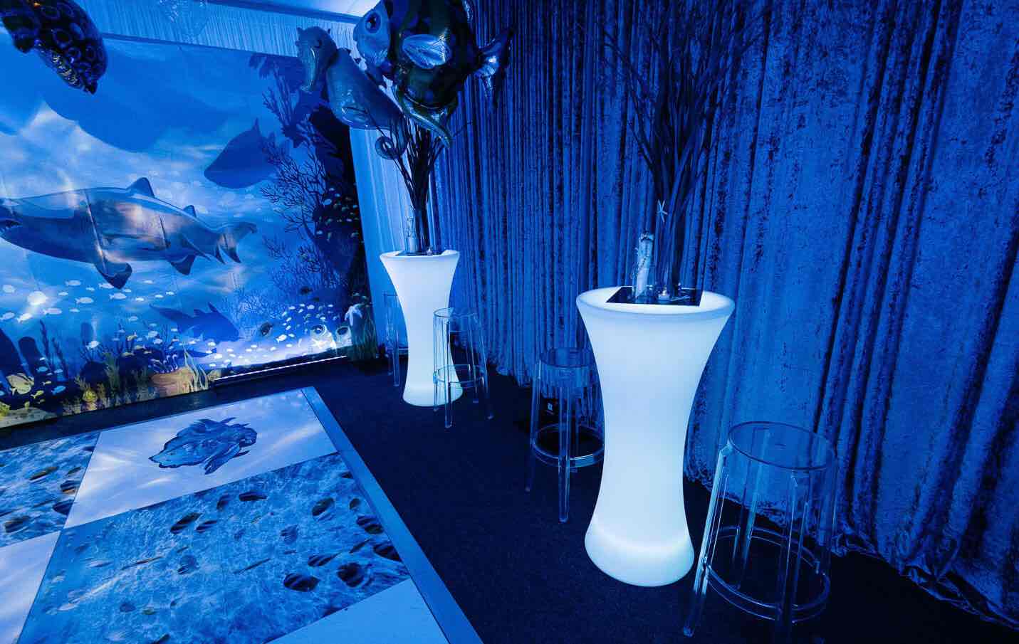 A room with vases and clear ghost stools against a blue background.