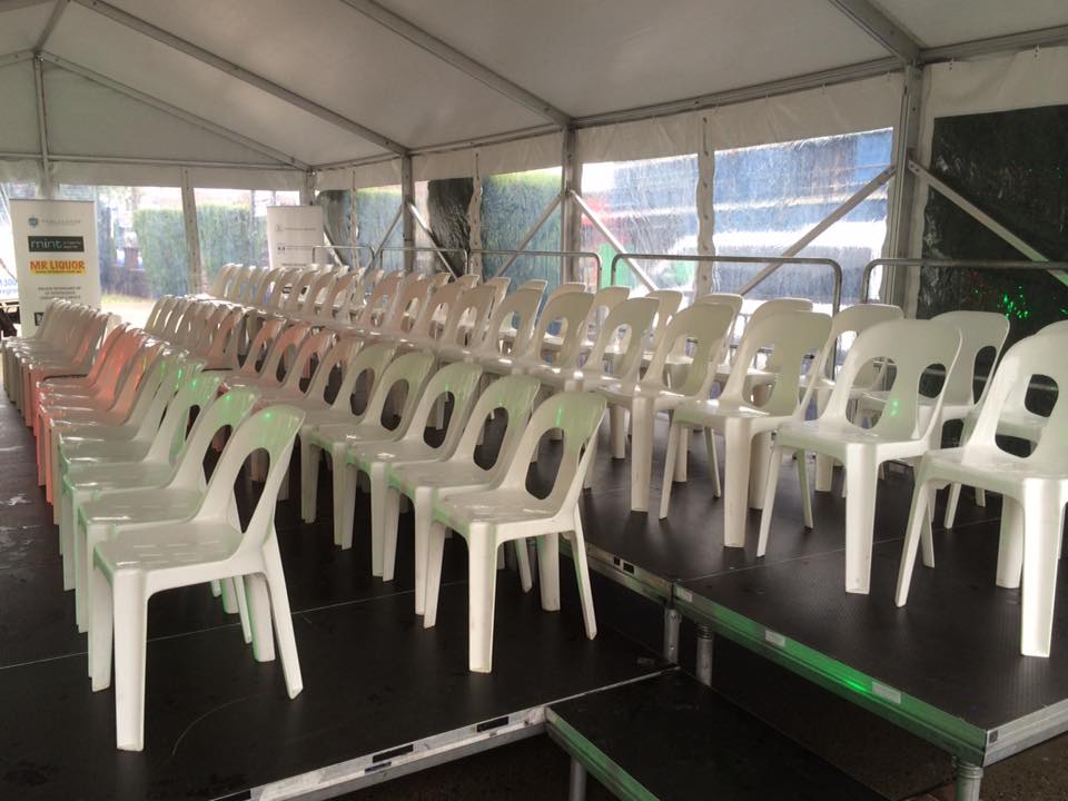 A row of stackable white plastic chairs available for hire in a tent.