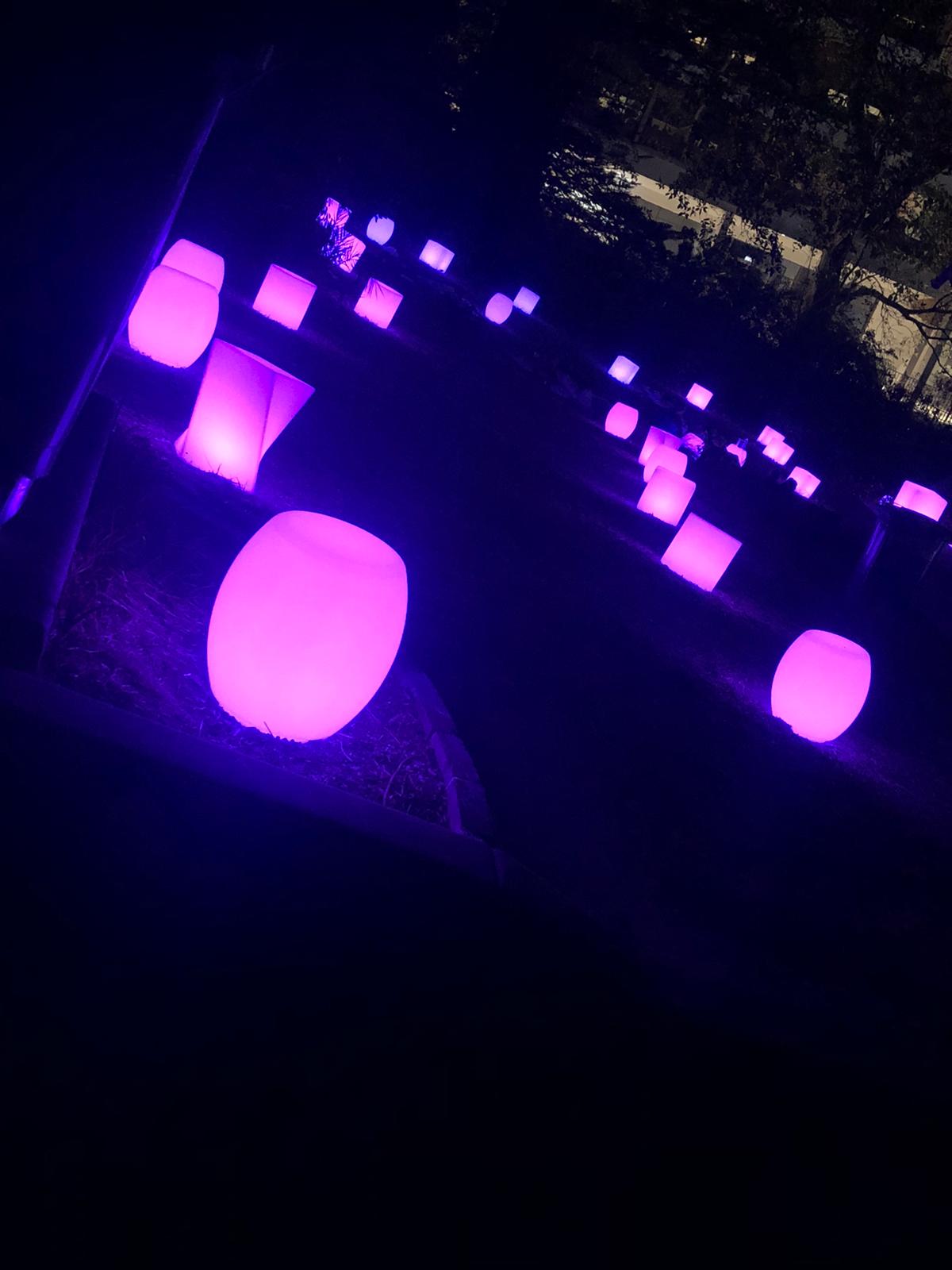 A group of purple stools in a dark area available for Glow Bongo Seat Hire.