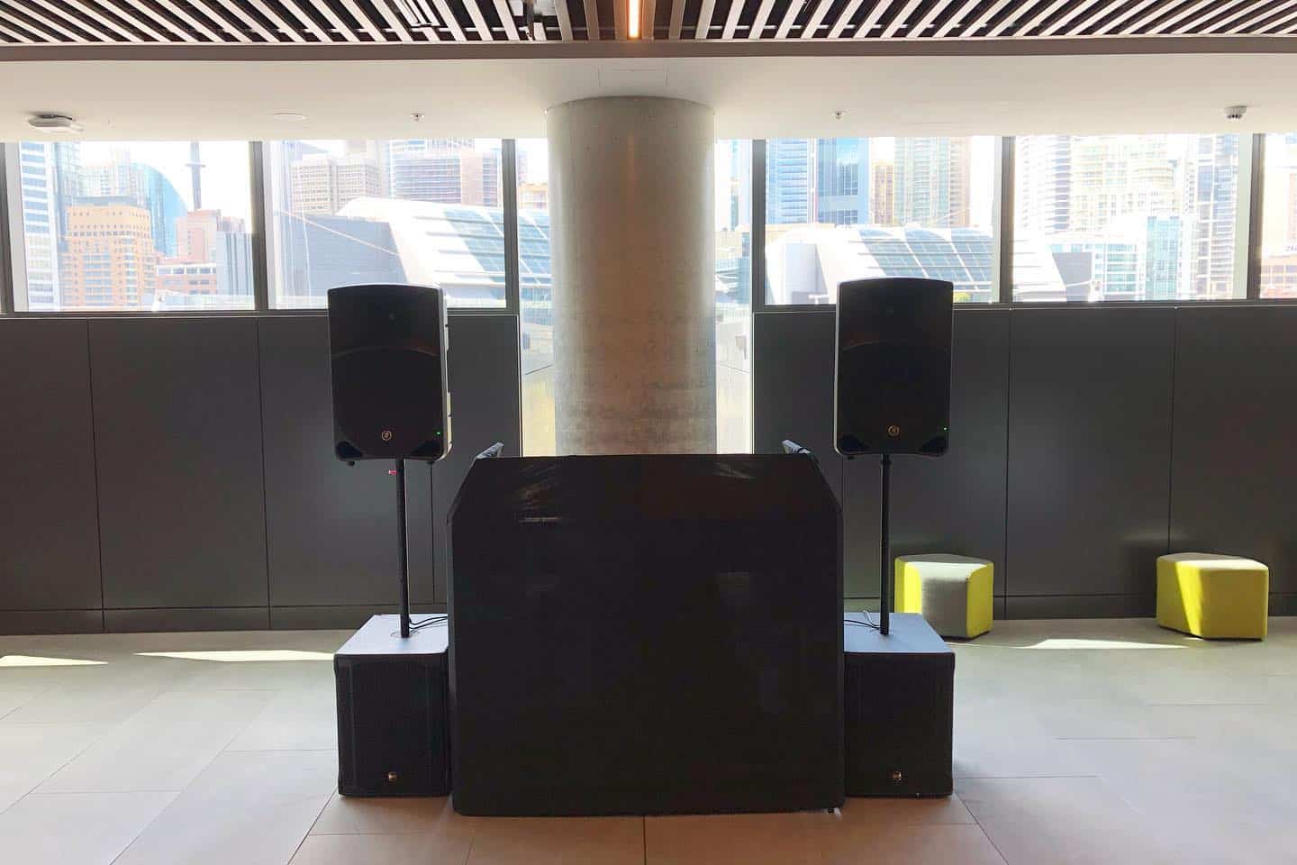 A room with two speakers on speaker stands in front of a large window available for hire.