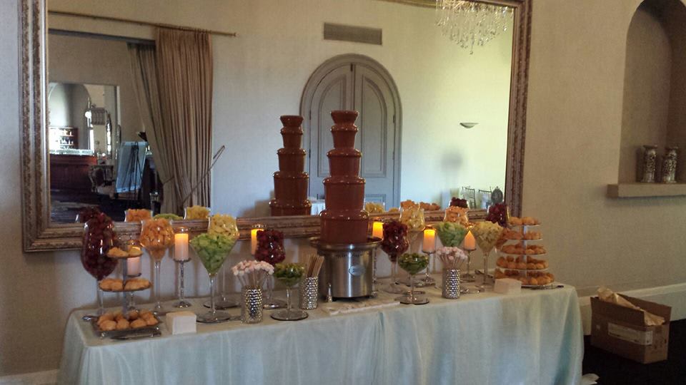 A large chocolate fountain is on a table in front of a mirror.