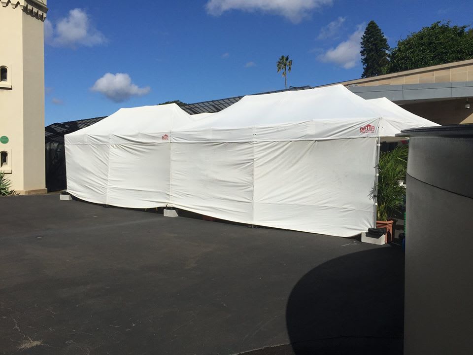 A white 3mx6m pop up marquee with walls on 3 sides is set up in front of a building.