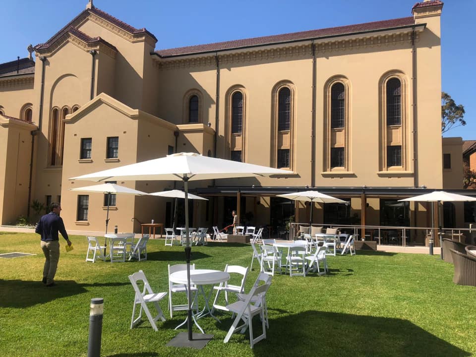 A large building with white tables and chairs in front of it, perfect for Market Umbrella Hire.