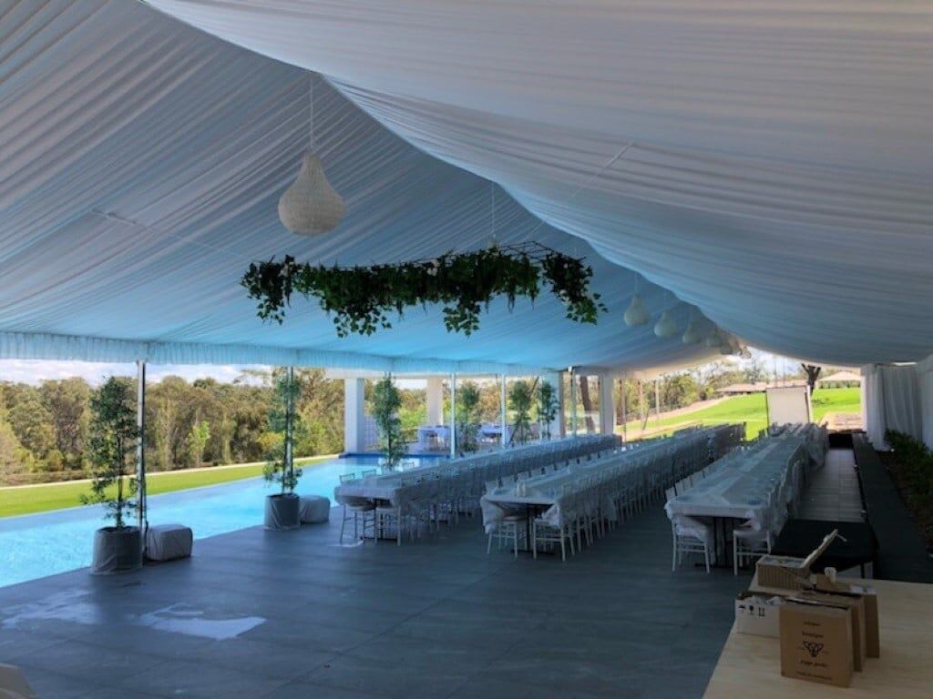 A white tent set up with tables and chairs illuminated by white pendant rope light.