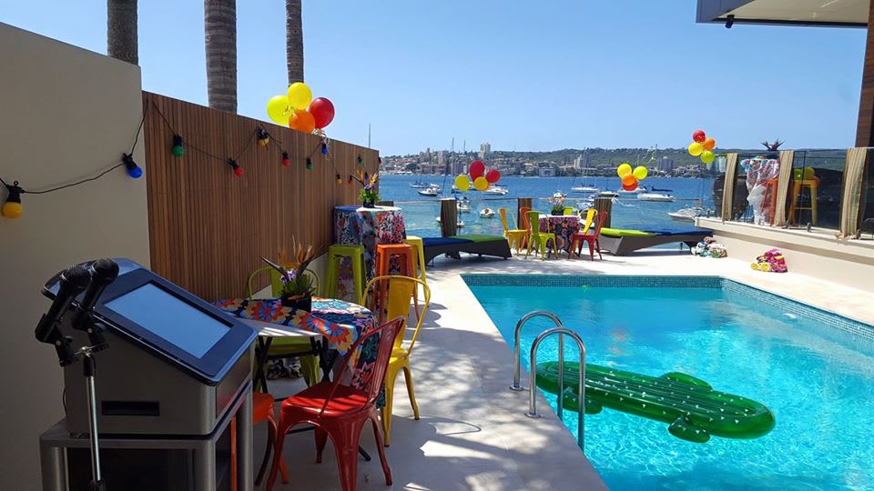 A lively pool party complete with a Jukebox & Karaoke Hire for added entertainment, where a table and chairs are conveniently placed near the water.