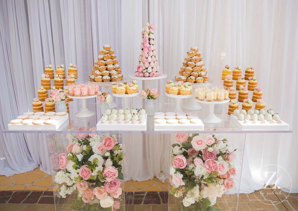 A dessert table adorned with cupcakes and flowers, featuring a Clear Acrylic Ghost Table.
