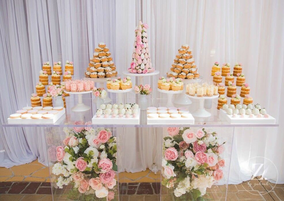 A dessert table adorned with cupcakes and flowers, featuring a Clear Acrylic Ghost Table.