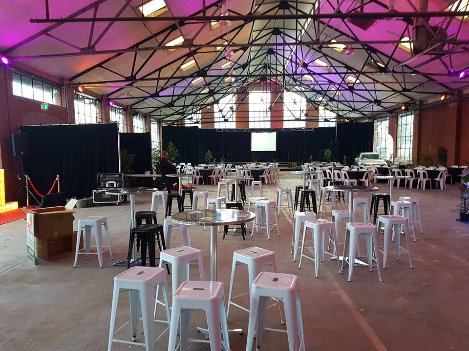 A large warehouse filled with tables, chairs, and white Tolix stool hire options.