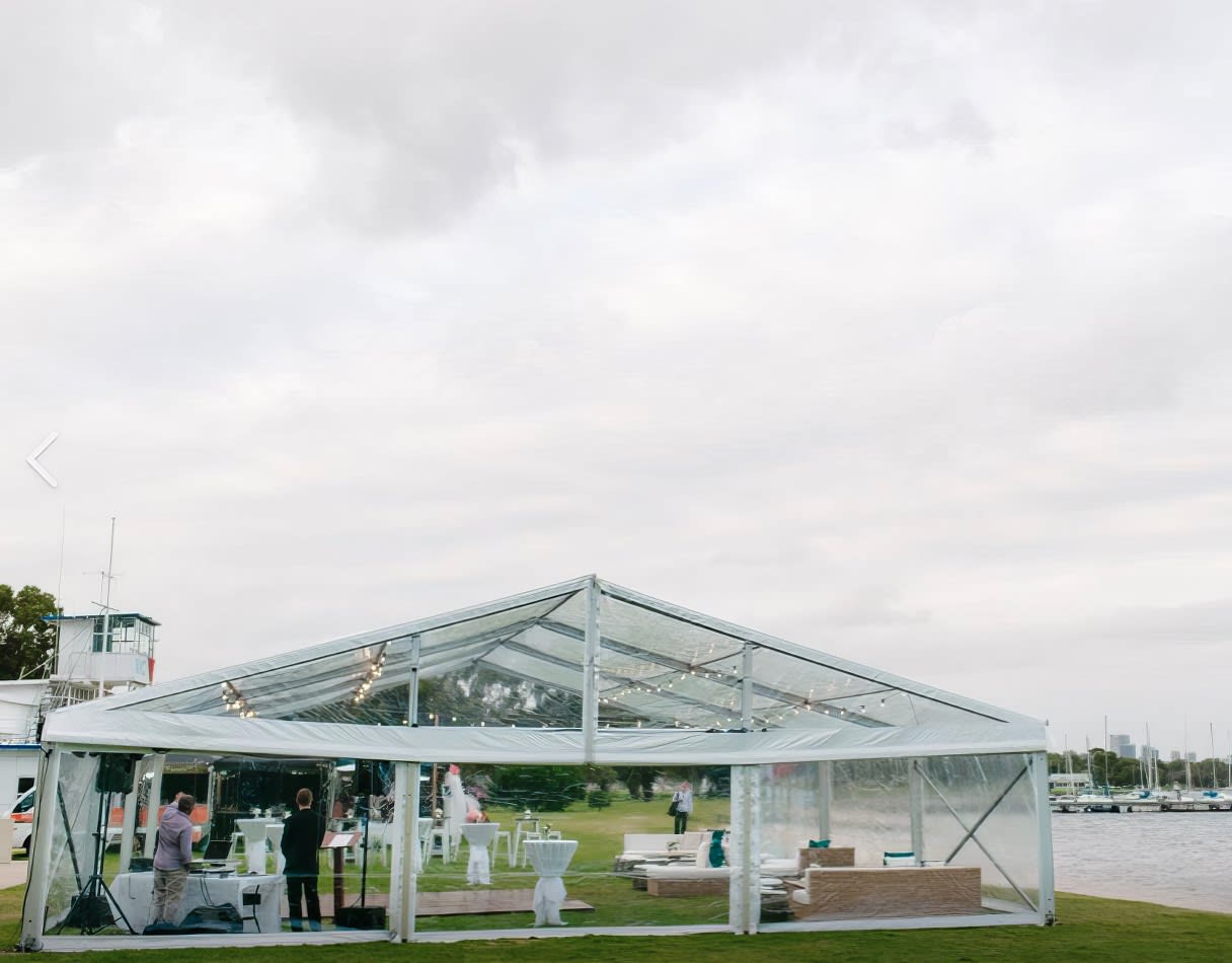 A framed marquee wedding tent set up on a grassy area near the water.