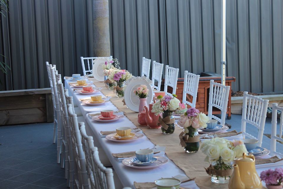 A tea party set up with a white tablecloth on a large trestle table.