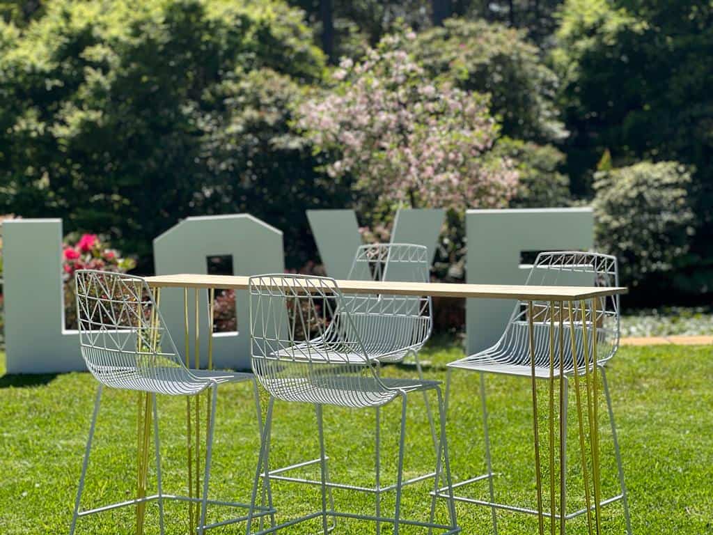 A high bar table with chairs and a love sign in the grass.