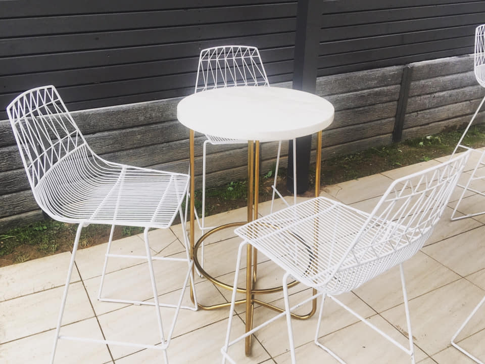 A set of white stools and a gold wire arrow table on a patio.