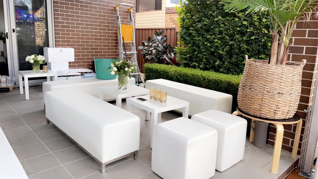 A patio with white furniture, including a white ottoman cube hire, and potted plants.