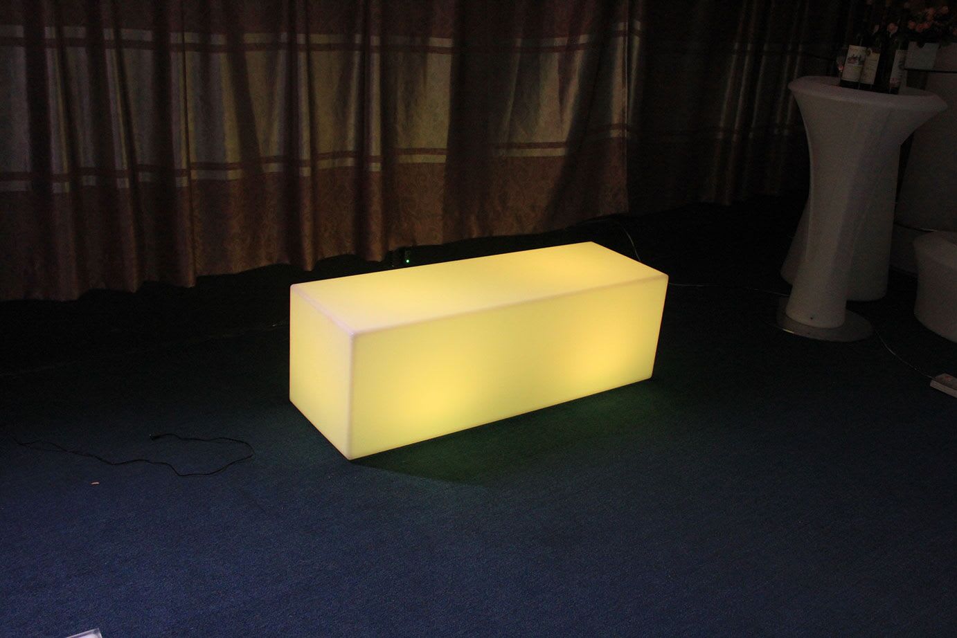 A yellow LED cube sitting on a carpeted floor, emitting a captivating glow.