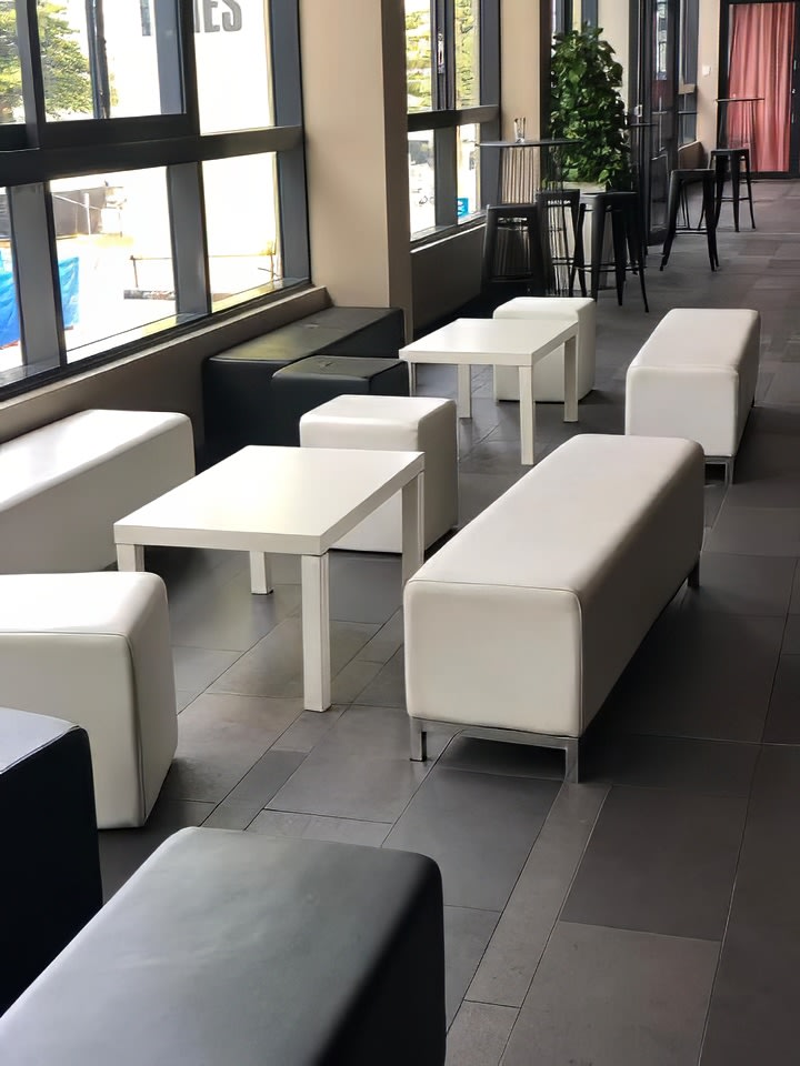 A group of white couches and tables in a lobby, accented with a black ottoman.