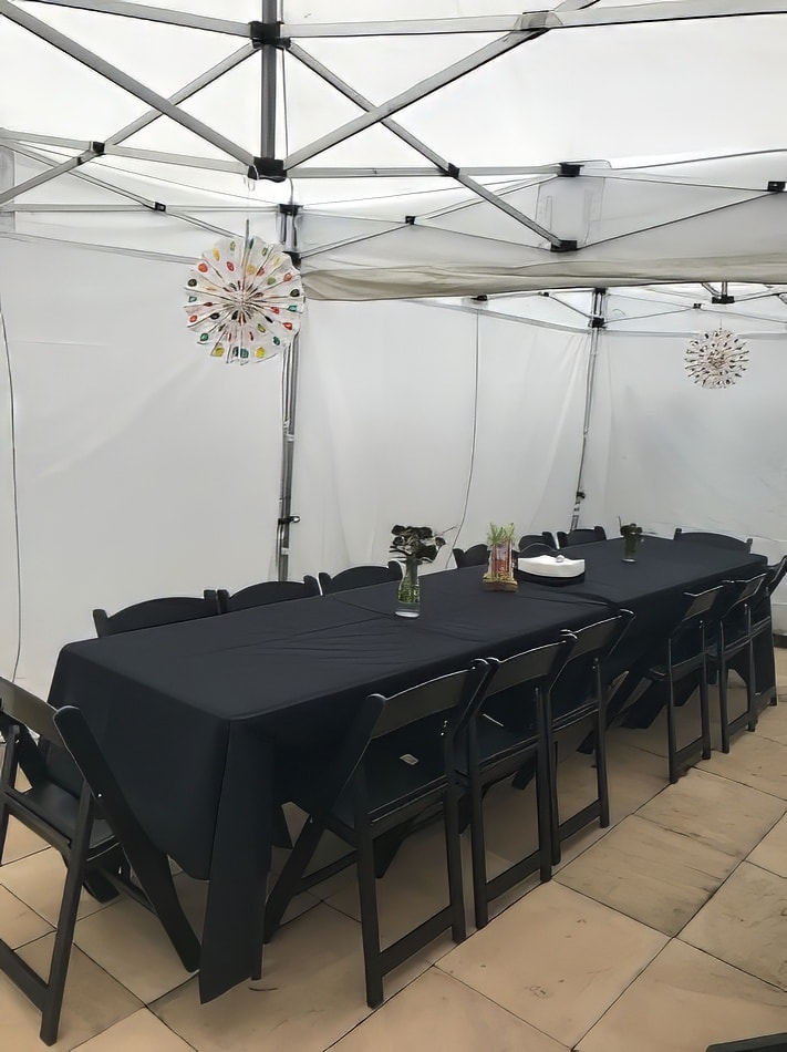 A table set up in a white tent with black chairs and a black tablecloth.