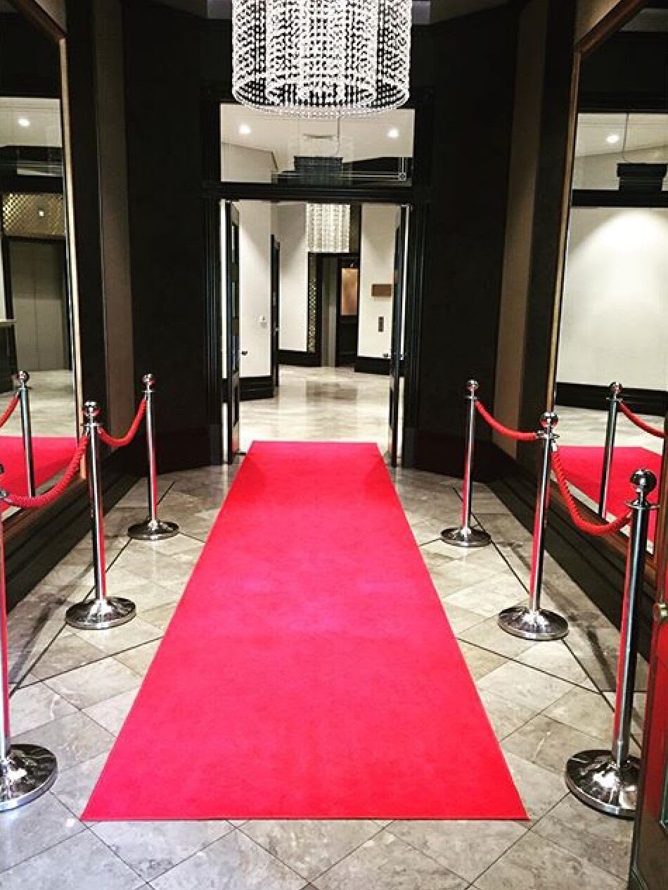 A red carpet leading into a building, flanked by sleek chrome bollards.