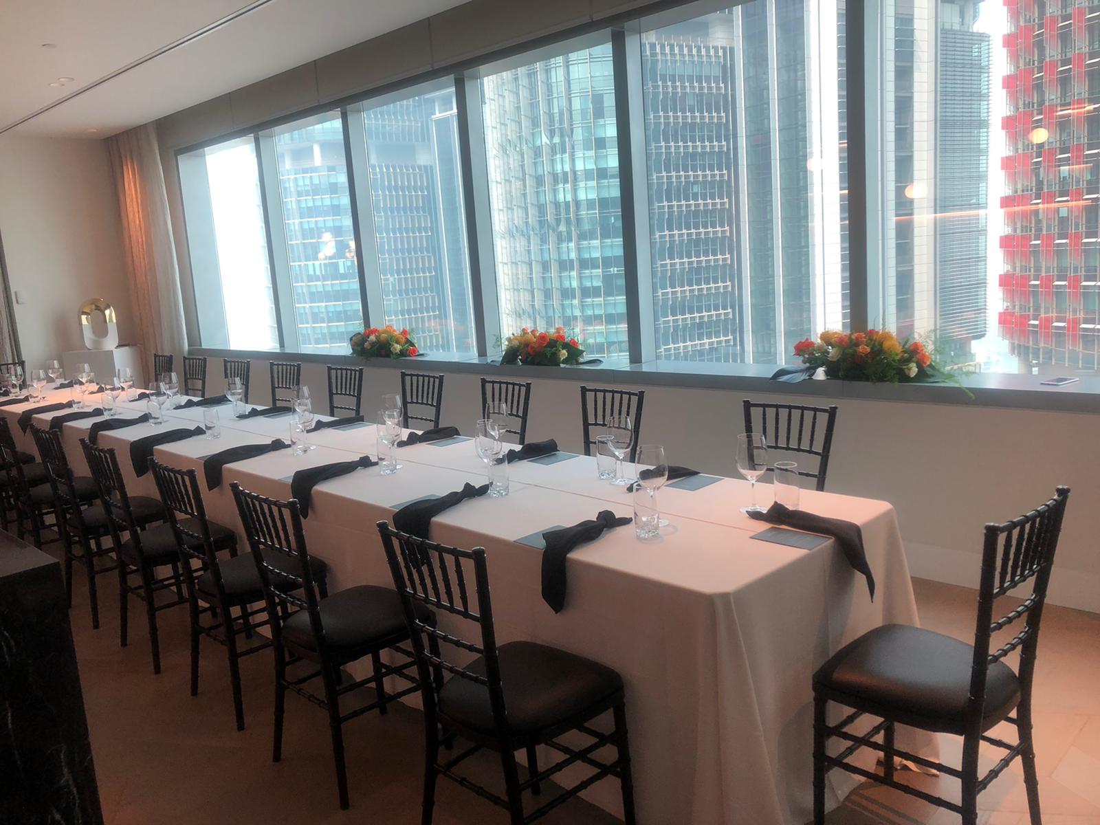 A table adorned with elegant black Tiffany chairs is set up in a room with a view of the city.