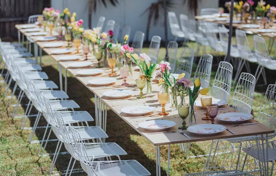 A Gold Hairpin Banquet Table w/ Timber Top set up with white chairs and flowers.