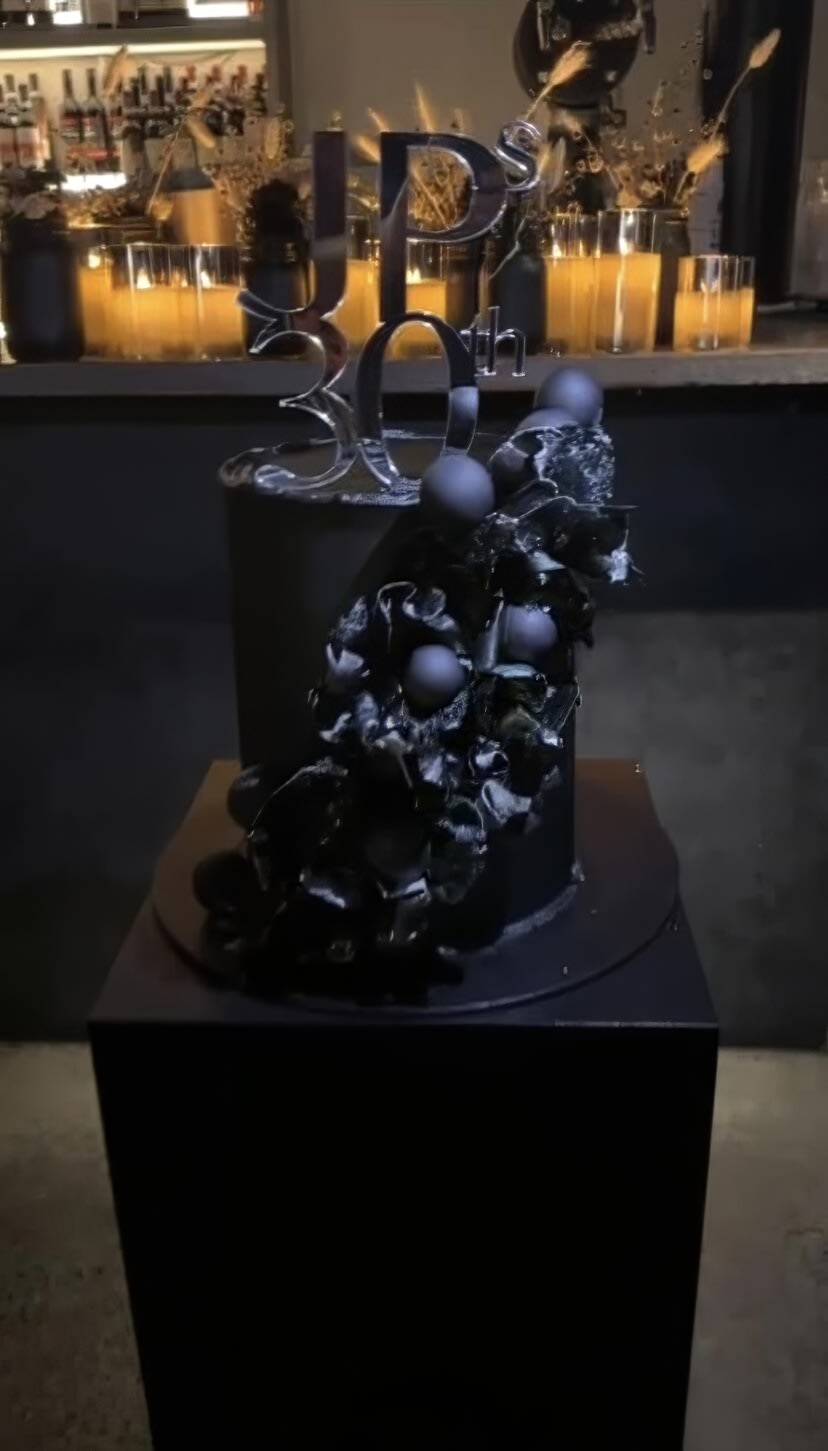 A black cake is on display on a large plinth in a bar.