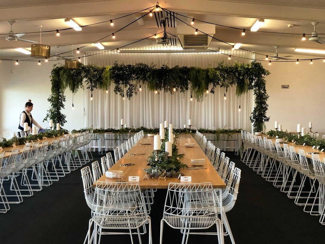 A room with tables and chairs set up for a wedding reception, featuring white arrow chair hire.