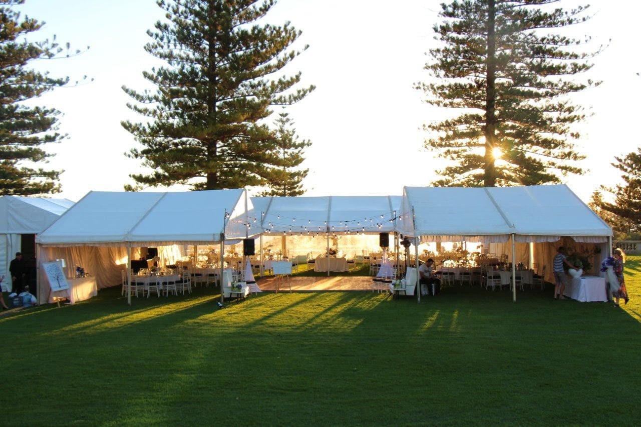 A white 8m x 21m framed marquee set up with tables and chairs on a grassy field.