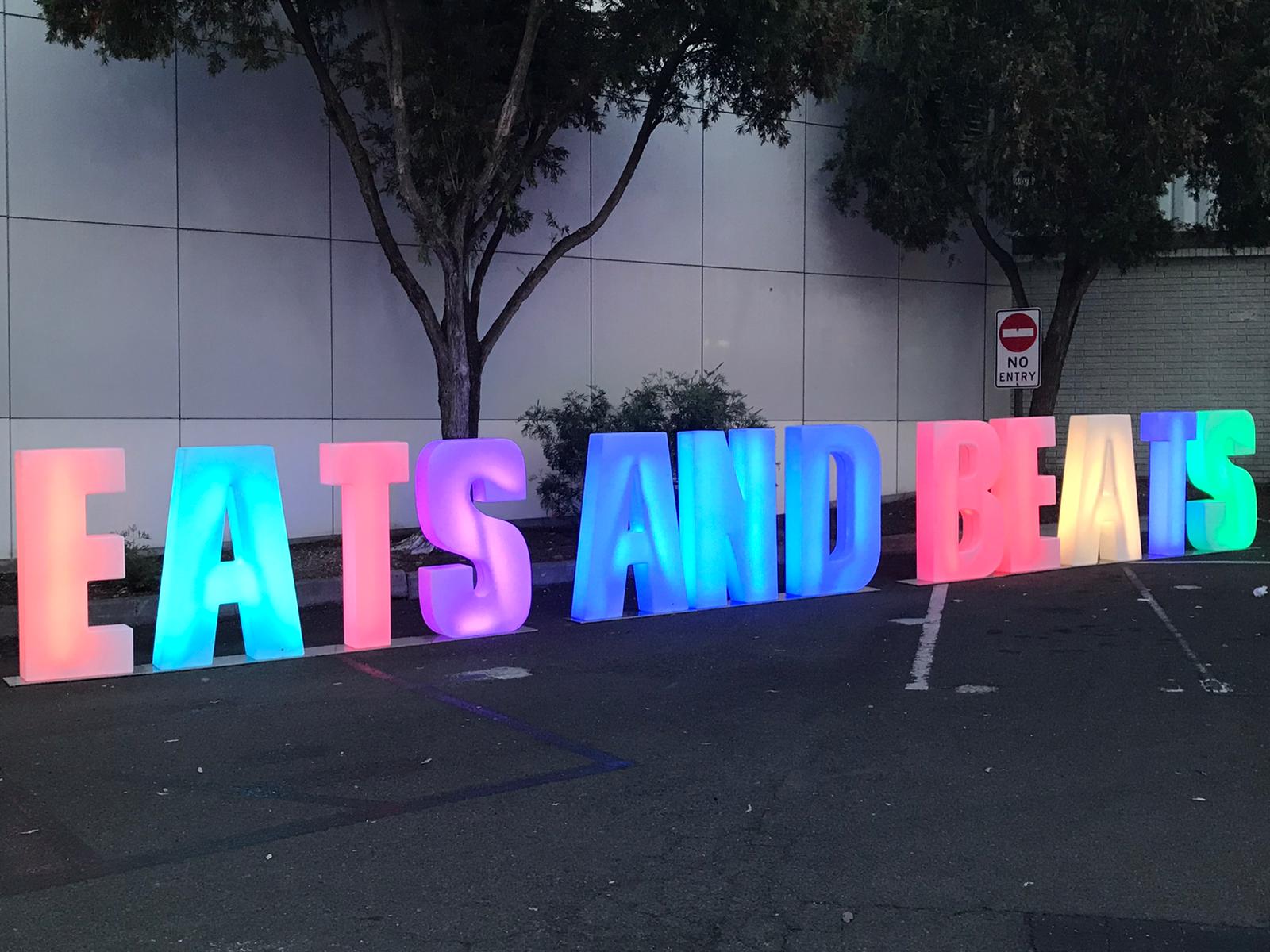 A sign with glow letters that says "eats and beats" in front of a parking lot.