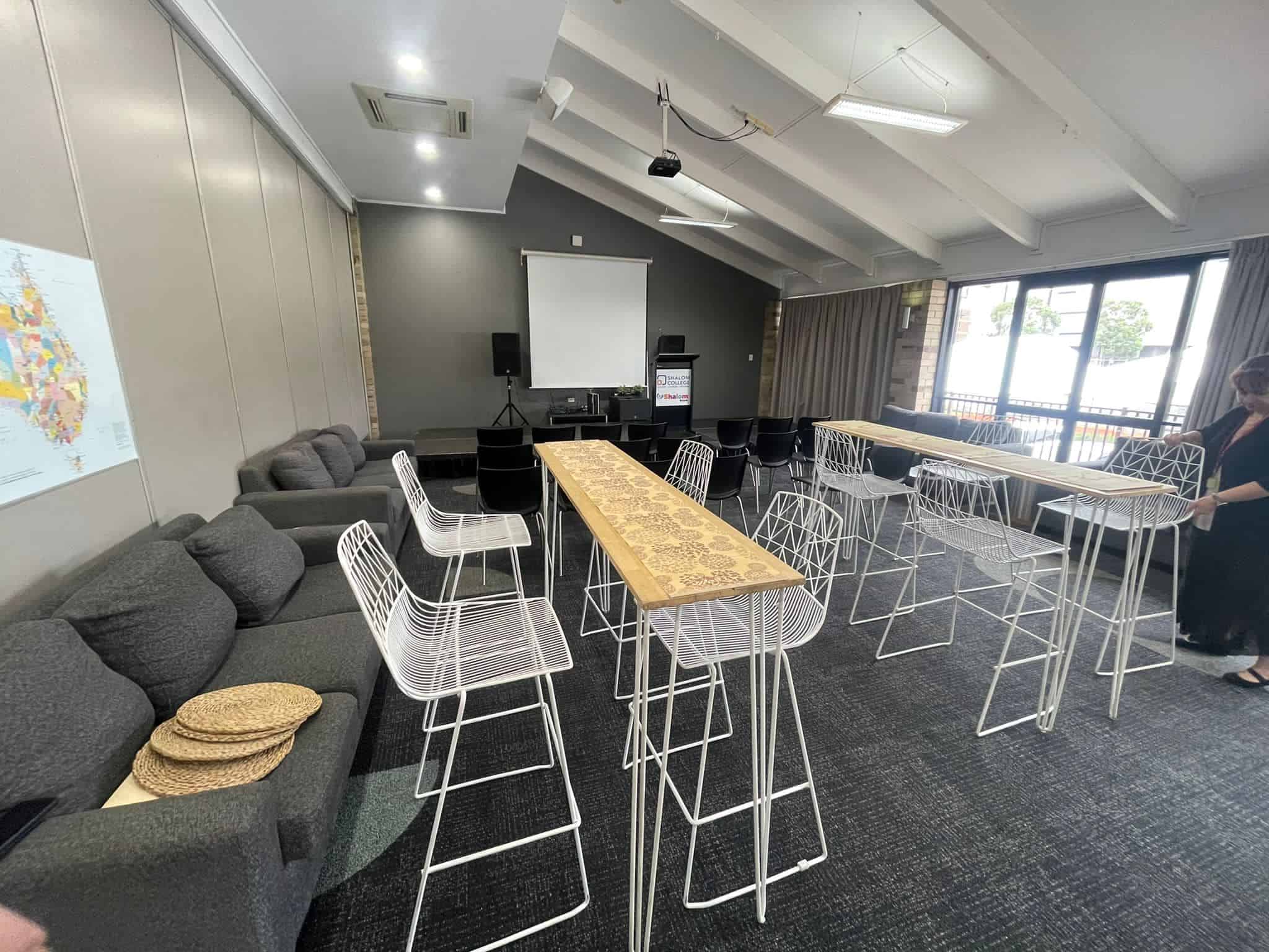 A room with white hairpin high bar tables and chairs with timber tops, and a projector.