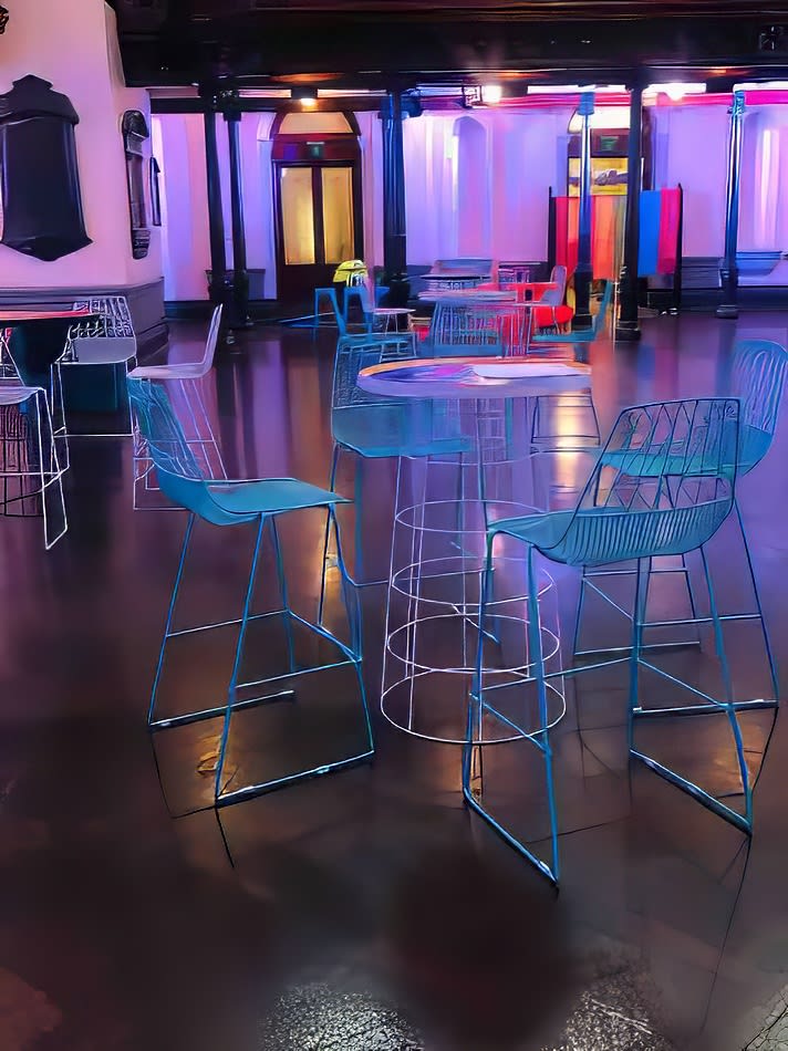 A room with turquoise wire stools and chairs in a dark room.