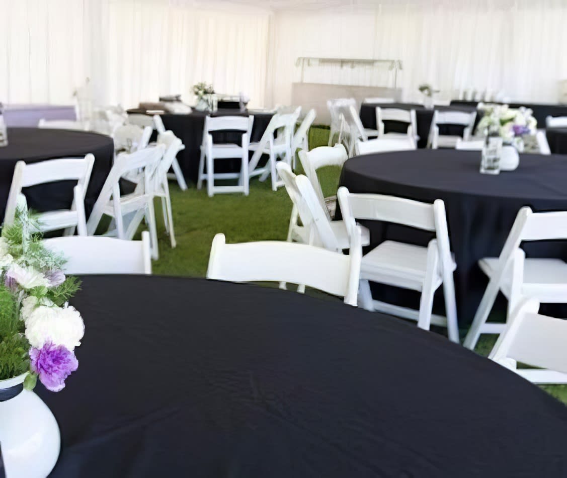 A white tent with black tables and chairs adorned with black round banquet tablecloths.