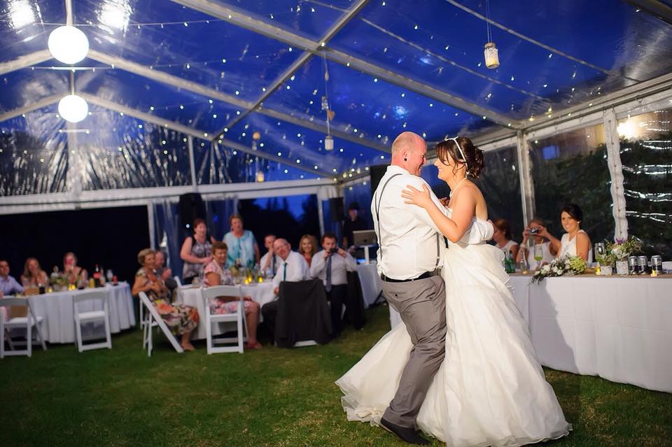 A bride and groom sharing their first dance under the romantic ambiance of white rice lanterns in a tent.
