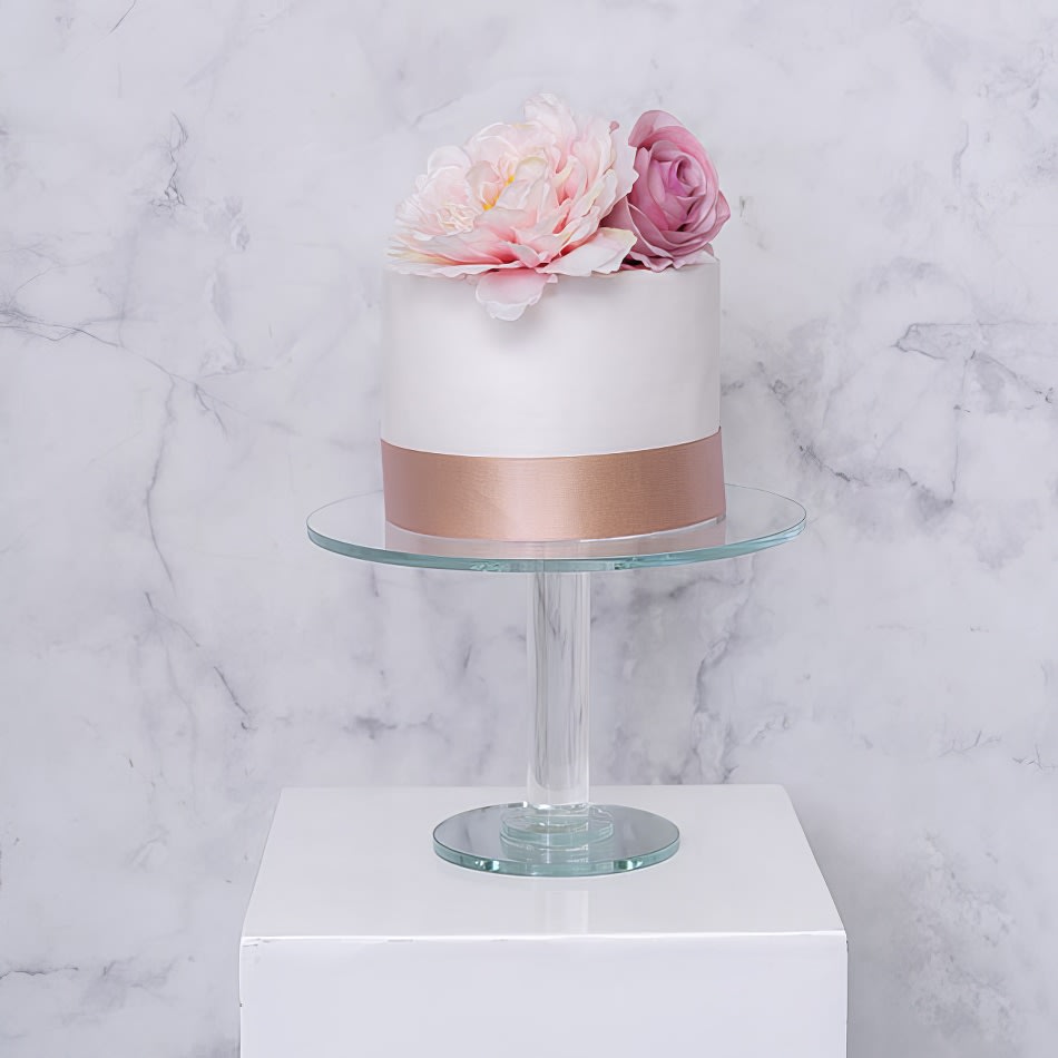 A white cake with pink flowers on a crystal cake stand.