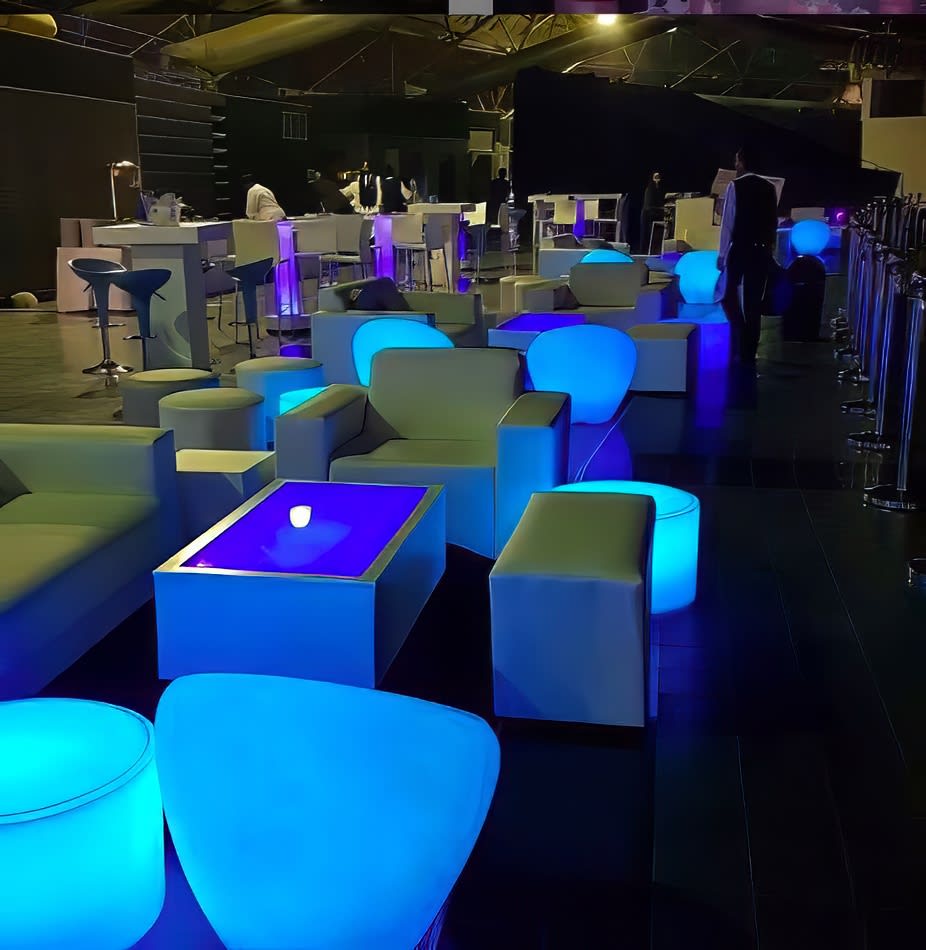 A stylish lounge area with mesmerizing blue and purple lighting, featuring a glamorous glow round ottoman hire.