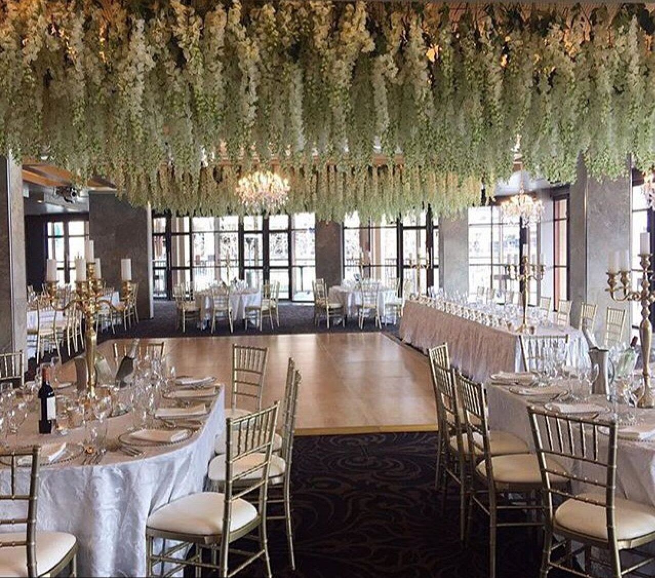 A wedding reception with white flowers hanging from the ceiling, complemented by elegant gold Tiffany chair hire.