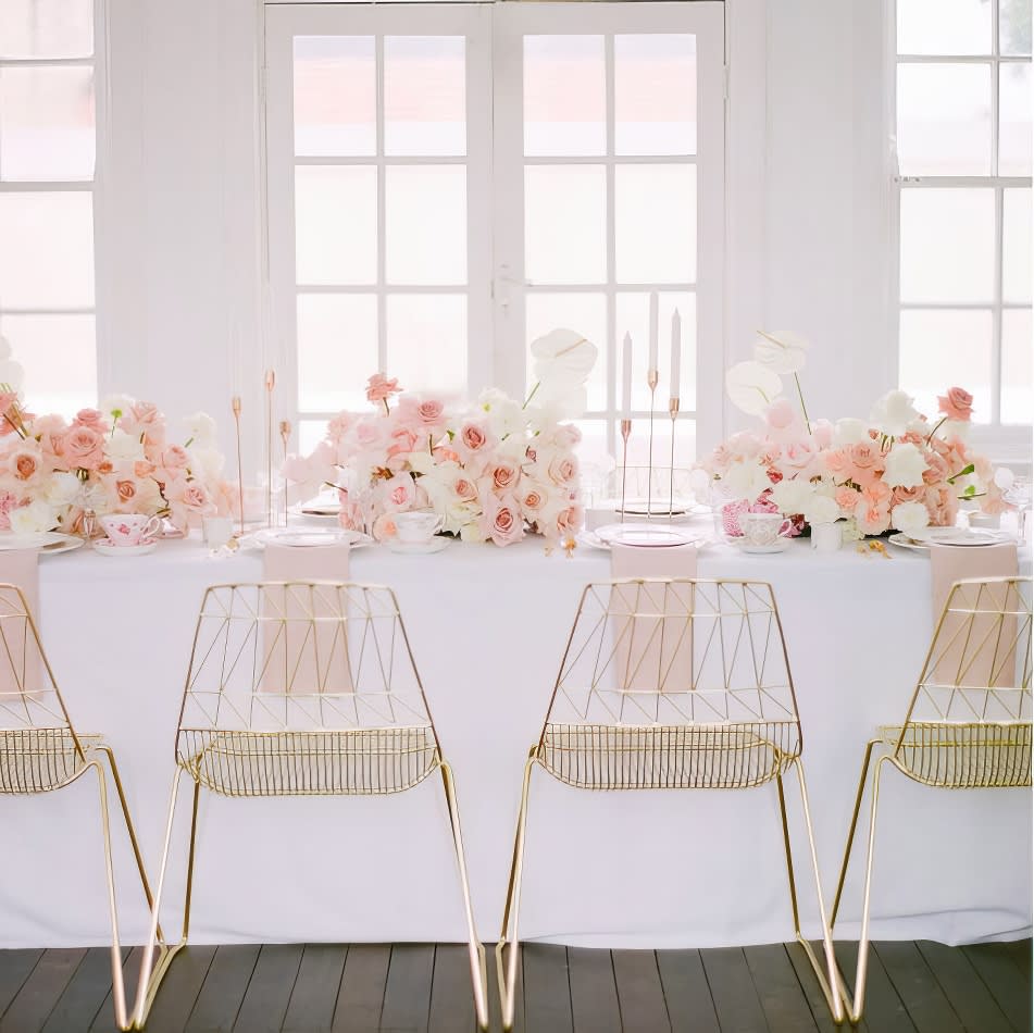 A white table adorned with pink flowers is paired elegantly with gold chairs.