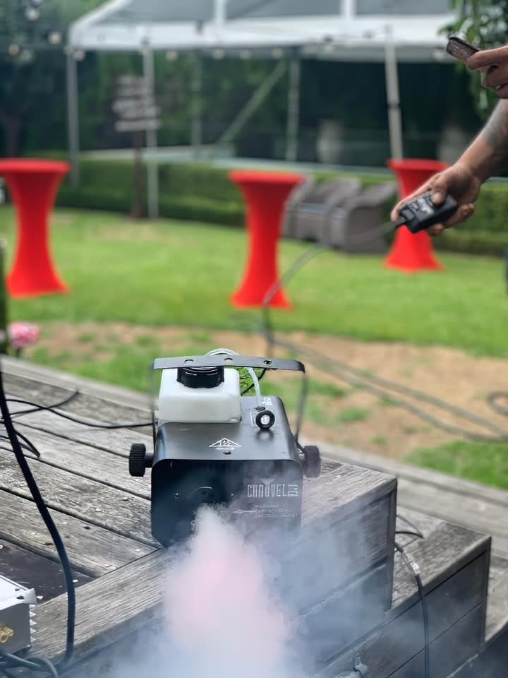 A man utilizing a smoke machine on a wooden deck for an unforgettable ambiance at a Smoke Machine Hire event.