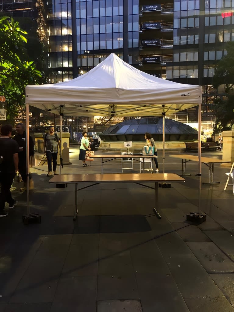 A white tent with tables and chairs in the middle of a city, featuring Timber Trestle Table 2.4m Hire setup.