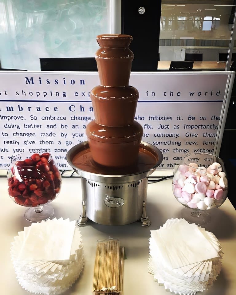 A medium commercial chocolate fountain on a table in a conference room.