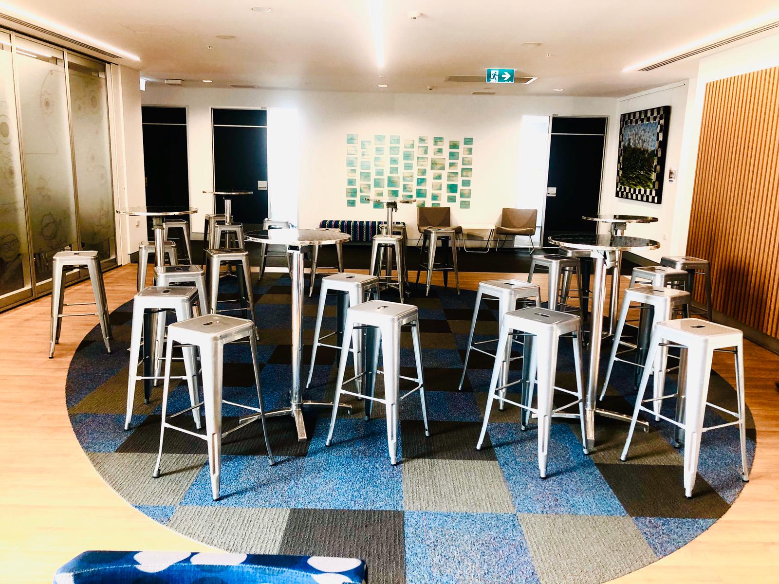 A group of stainless steel cocktail bar tables in a room with a blue checkered floor.