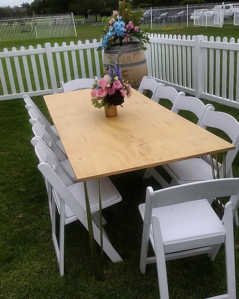 A white table with chairs in a grassy area, adorned with a gold hairpin banquet table with a timber top.