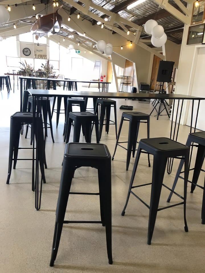 A spacious room furnished with sleek black Tolix stools and tables.